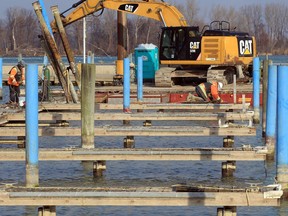 Using torches, workers with Facca Inc. remove horizontal landing walkways from the vertical pilings at Lakeview Park Marina. The stationary docks are being removed to be replaced by floating ones due to high water levels. The crane seen here is sitting on a barge.