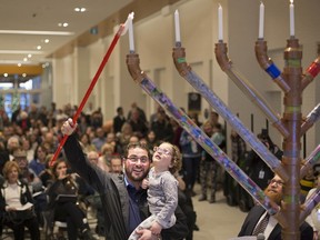 Mark Abraham, president of the Windsor Jewish Federation, with his daughter, Lilah, 4, lights the first light on the menorah to the mark the beginning of Hanukkah, while at Devonshire Mall on Dec. 22, 2019.