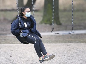 A woman wears a surgical mask while on a swing at the McKee Park in Windsor, ON. on Thursday, March 19, 2020.