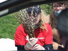 From a safe distance, a motorist on Thursday, April 9, 2020, is shown a handful of pussy willows held by Lauren Snyder-Gault, left, with her daughter Jasmin Gault looking on during their Save the Children Canada fundraiser. It's usually run through the Tecumseh United Church, but COVID-19 has changed that.