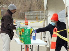 Windsor, Ontario. April16, 2020.  Stephen Jones, 65, centre, receives groceries from volunteers at the new Drive Thru Food Bank Hub at St. Michael's Adult Secondary School in West Windsor Thursday.  The drive thru food hub was set up by Mike Turnbull (not shown), Food Rescue Manager at the Unemployed Help Centre of Windsor to meet the growing demand of those requiring food assistance safely during the COVID-19 pandemic.  A walkup area was available for those receiving food on foot using a conveyor to maintain social distancing.