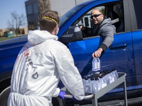 Wolfhead Distillery staff members distribute 350ml bottles of hand sanitizer, 2000 of which were produced at the distillery for the fight against COVID-19, Friday, April 3, 2020.  Cars lined up down Howard Avenue to pick up their 2-bottle limit. The distillery was offering them up for free.