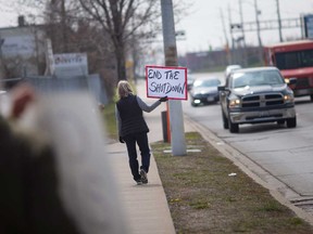 Protester Constance Thomson holds up a sign at Walker Road and Ottawa Street in Windsor on April 24, 2020.
