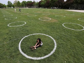A girl sits in a field where circles were painted to help visitors maintain social distancing to slow the spread of the coronavirus disease (COVID-19) at Trinity Bellwoods park in Toronto on May 28, 2020.