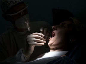 A dentist wearing protective equipment treats a patient in his dental clinic in Guebwiller, eastern France, on May 20, 2020.