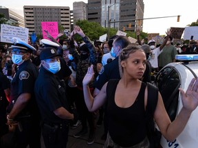 Protesters hold their hands up and chant hands up dont shoot. while Detroit Police officers look on, during a protest in the city of Detroit, Michigan, on May 29, 2020, over the death of George Floyd, a black man who died after a white policeman knelt on his neck for several minutes. - Violent protests erupted across the United States late on May 29, over the death of a handcuffed black man in police custody, with murder charges laid against the arresting Minneapolis officer failing to quell boiling anger.