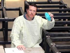 Andrew Glover, co-owner of Harbour Technologies, is surrounded by steel bases, part of an automation assembly operation for all-Canadian production of PPE. Glover is shown wearing a prototype PPE gown and holding a prototype N-95 mask.