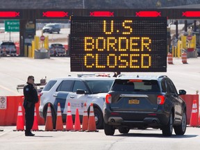 In this file photo US Customs officers speaks with people in a car beside a sign saying that the US border is closed at the US/Canada border in Lansdowne, Ontario, on March 22, 2020.