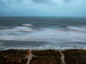 Large surf is swirled by the wind and captured by a long exposure, while a person stands on the shore as Hurricane Isaias approaches North Myrtle Beach, SC on August 3, 2020.