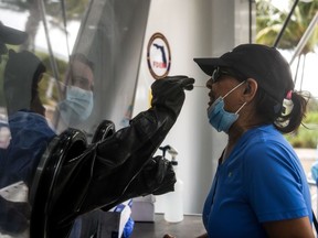 In this file photo taken on July 24, 2020, nurse practitioner Raciel Gomez (L) swabs the nose of Jeewan Prabha Mehta through a glass pane at the Aardvark Mobile Health's Mobile Covid-19 Testing Truck in Miami Beach.