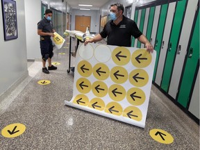 New direction due to COVID-19. Custodians James Pomponio, left, and Ron Galipeau, both with the Greater Essex County District School Board, are shown Aug. 25, 2020, applying directional and distancing stickers to floors at W. F. Herman Academy.