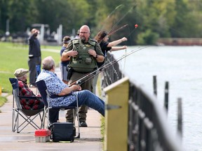 Checking on the fishing action, Ontario Ministry of Natural Resources conservation officer Sean Insley, centre, talks with anglers at Alexander Park on Riverside Drive East in Windsor on Monday, Sept. 7, 2020. Insley was busy on Labour Day, driving along the Windsor and Tecumseh waterfronts.  Conservation officers have authority to go on private property to do their jobs, so fishers in private marinas and docks must comply with the rules. Not having a valid fishing licences is costly.  Insley handed out two $155-tickets earlier in the day. A three-year sport fishing licence and outdoors card costs less than $90.