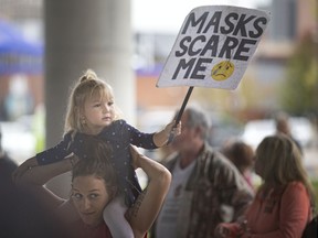 A young girl holds a 'Masks scare me' sign as protesters opposed to wearing masks rally outside city hall during a city council meeting, Monday, September 28, 2020.