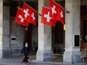 A woman passing by Swiss flags wears a mask in the street ahead of the announcement by the government of new restrictions to fight the COVID-19 outbreak in Bern, on October 27, 2020.