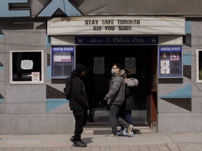 Pedestrians wearing masks walk past a closed music venue on Queen St. on March 25, 2020. Photographer: Cole Burston/Bloomberg