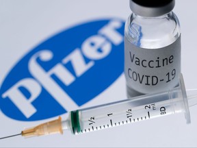 This illustration picture shows a syringe and a bottle reading "Covid-19 Vaccine" next to the Pfizer company logo.