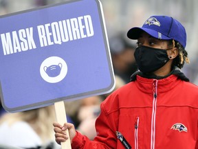 A member of M&T Bank Stadium security holds up a sign reminding patrons to wear masks during a game between the Pittsburgh Steelers amd Baltimore Ravens.