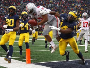 J.K. Dobbins of the Ohio State Buckeyes dives for a fourth quarter touchdown past Josh Metellus of the Michigan Wolverines at Michigan Stadium on November 30, 2019 in Ann Arbor, Michigan.