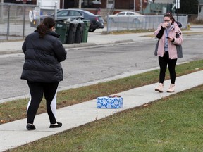 Wearing masks and carrying sanitizer, friends Christina Bourgoin, left, and Maggie Duvnjak exchange Christmas gifts on a stretch of Langlois Avenue sidewalk on Monday, Dec. 21, 2020. Both gifts were wiped down with sanitizer and the friends kept a safe distance apart during the transaction.