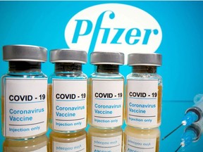 Vials with a sticker reading, "COVID-19 / Coronavirus vaccine / Injection only" and a medical syringe are seen in front of a displayed Pfizer logo in this illustration taken October 31, 2020.