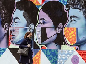 A pedestrian wearing a mask walks past Street Art Toronto by artist Cindy Scaife in support of Frontline workers at the corner of Bloor Street West and Dundas Street West in Toronto during the Covid 19 pandemic, Thursday December 3, 2020.