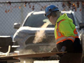 A construction worker exhales while cutting plywood at a job site off Roblin Boulevard in Winnipeg on Dec. 2, 2020.