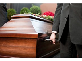 Funeral with coffin on a cemetery, the casket carried by a funeral director.