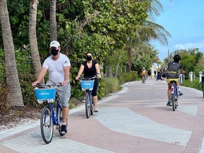 Tourists wear masks as they bike along the beach in Miami, Dec. 20, 2020, amid the COVID-19 pandemic.