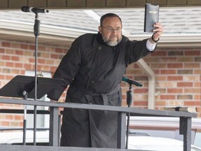 Church of God Pastor Henry Hildebrandt holds up a copy of the Bible on a stage in the Aylmer area church's parking lot in April. Some townspeople are fighting back against his stand against pandemic restrictions by protesting across the road from the church. (Derek Ruttan/The London Free Press)