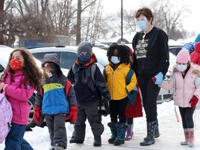 Wearing a face shield and mask, a St. John Vianney Catholic Elementary School staffer helps children board the bus after school Monday.