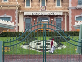 An employee cleans the grounds behind the closed gates of Disneyland Park on the first day of the closure of Disneyland and Disney California Adventure theme parks on March 14, 2020.