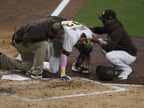 A trainer and manager Jayce Tingler (R) look on as Fernando Tatis Jr. of the San Diego Padres grimaces in pain after taking a swing during the third inning of a baseball game against the San Francisco Giants at Petco Park on April 5, 2021 in San Diego, California.
