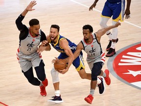 Stephen Curry of the Golden State Warriors dribbles in front of Daniel Gafford and Ish Smith of the Washington Wizards during the second half at Capital One Arena on April 21, 2021 in Washington, DC.