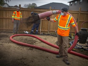 Korey Kelch of Quality Turf, one of several landscaping companies involved, sprays top soil from a giant tube at the residence of Dan and Megan Monk in Amherstburg, on Saturday, April 24, 2021.  The couple won a garden makeover awarded to frontline workers from Landscape Ontario.