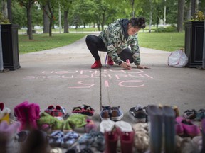 Ashlie Sandy writes a message with chalk at a makeshift memorial on the steps of Our Lady of Assumption Church to honour the 215 indigenous children found in a mass grave at a residential school in Kamloops, on Monday, May 31, 2021.