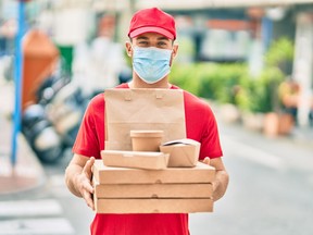 Young caucasian deliveryman wearing medical mask  holding delivery food at the city.