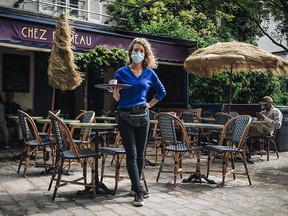 A waitress poses in front of the terrace of her cafe in Paris on May 19 2021, as restaurant and bar terraces re-open as part of an easing of the nationwide lockdown due to the Covid-19 pandemic.