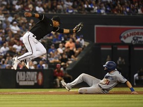 Eduardo Escobar of the Arizona Diamondbacks makes a leaping catch on a wild throw from Christian Walker as AJ Pollock of the Los Angeles Dodgers slides into third base at Chase Field on June 19, 2021 in Phoenix, Arizona. Walker Buehler of the Dodgers was safe at first base on a fielders choice and an error by Christian Walker.