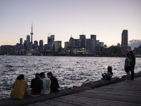 People sit on a dock along the skyline during sunset in Toronto, Ontario, Canada, on Saturday, June 19, 2021.