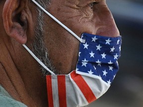 (FILES) In this file photo taken on July 19, 2021, a man wears an American flag face mask on  a street in Hollywood, California, on the second day of the return of the indoor mask mandate in Los Angeles County due to a spike in coronavirus cases. - With the Delta variant pushing US Covid cases back up, fully vaccinated people are wondering whether they need to start masking indoors again. Covid vaccines remain extremely effective against the worst outcomes of the disease -- hospitalization and death -- and breakthrough infections remain uncommon.