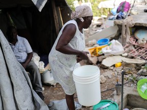 Wisner Desrosier, 67, carries a bucket next to her husband Manithe Simon, 68, outside their collapsed home in Marceline near Lea Cayes, Haiti, Aug. 22, 2021.