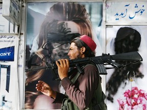 A Taliban fighter walks past a beauty saloon with images of women defaced using spray paint in Shar-e-Naw in Kabul on August 18, 2021.