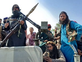Taliban fighters sit over a vehicle on a street in Laghman province on Aug. 15, 2021.
