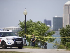 A Windsor police officer puts up yellow tape to contain a scene where emergency crews responded to a person in the water in the Detroit River near the base of Moy Avenue on Thursday. The man has since died.