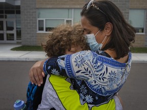 Randa Kumail hugs her twelve-year-old son, Anas Shebli, a Grade 7 student at the new Legacy Oak Trail public school, while her oldest son, Omar, a Grade 9 student at Sandwich Secondary School, looks on after the first day of school ended, on Tuesday, September 7, 2021.