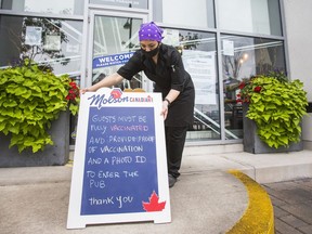 Kitchen manager Fernanda Tavarese 
is seen with a notice of Ontario's new vaccination requirement on a sandwich board at Firkin on the Bay pub in the Humber Bay Shores neighbourhood in Toronto on Sept. 21, 2021.