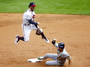 Dansby Swanson of the Atlanta Braves turns a double play during the eighth inning over Willy Adames of the Milwaukee Brewers  in game 3 of the National League Division Series at Truist Park on October 11, 2021 in Atlanta, Georgia.