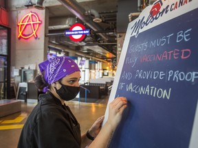 Kitchen manager Fernanda Tavares writes a notice of Ontario's new vaccination requirement on a sandwich board at Firkin on the Bay pub in the Humber Bay Shores neighbourhood in Toronto on Tuesday September 21, 2021.