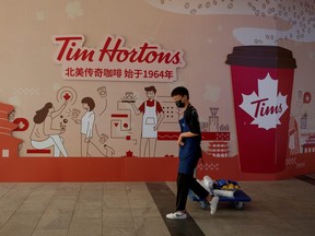 A man walks past a store front poster advertising the opening of a cafe of the Canadian coffee and fast food chain Tim Hortons in Beijing, July 6, 2020.