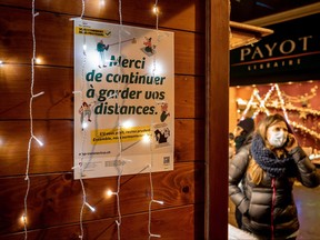 A woman, wearing a face mask as a preventive measure against COVID-19, walks past a placard reading in French: "Please continue to keep your distance" in a Christmas market in Lausanne on Dec. 2, 2021.